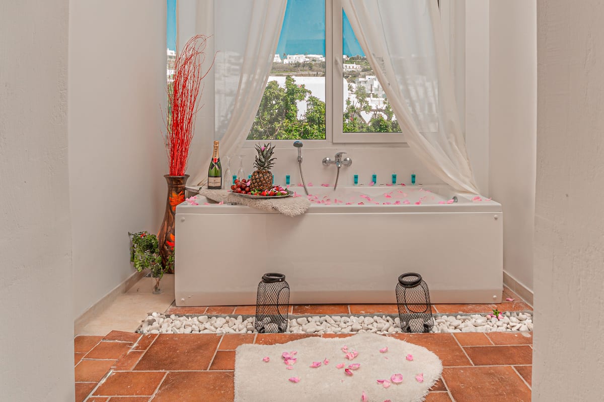 A bathroom with a bathtub, a window with curtains, a bottle of champagne, and a pineapple on the counter.