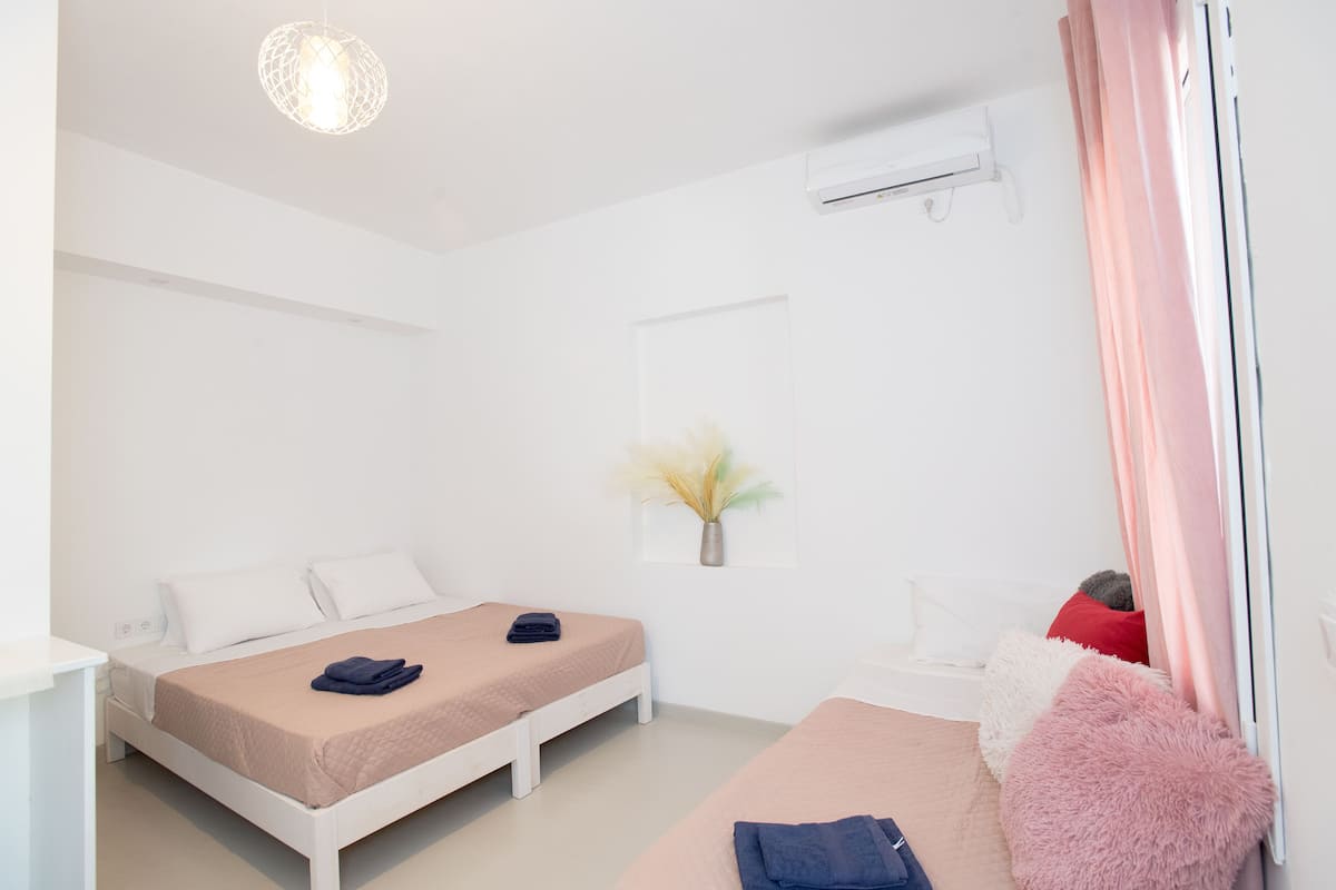 A modern bedroom with two beds, a white air conditioning unit, a wall-mounted vase, and a window with pink curtains.