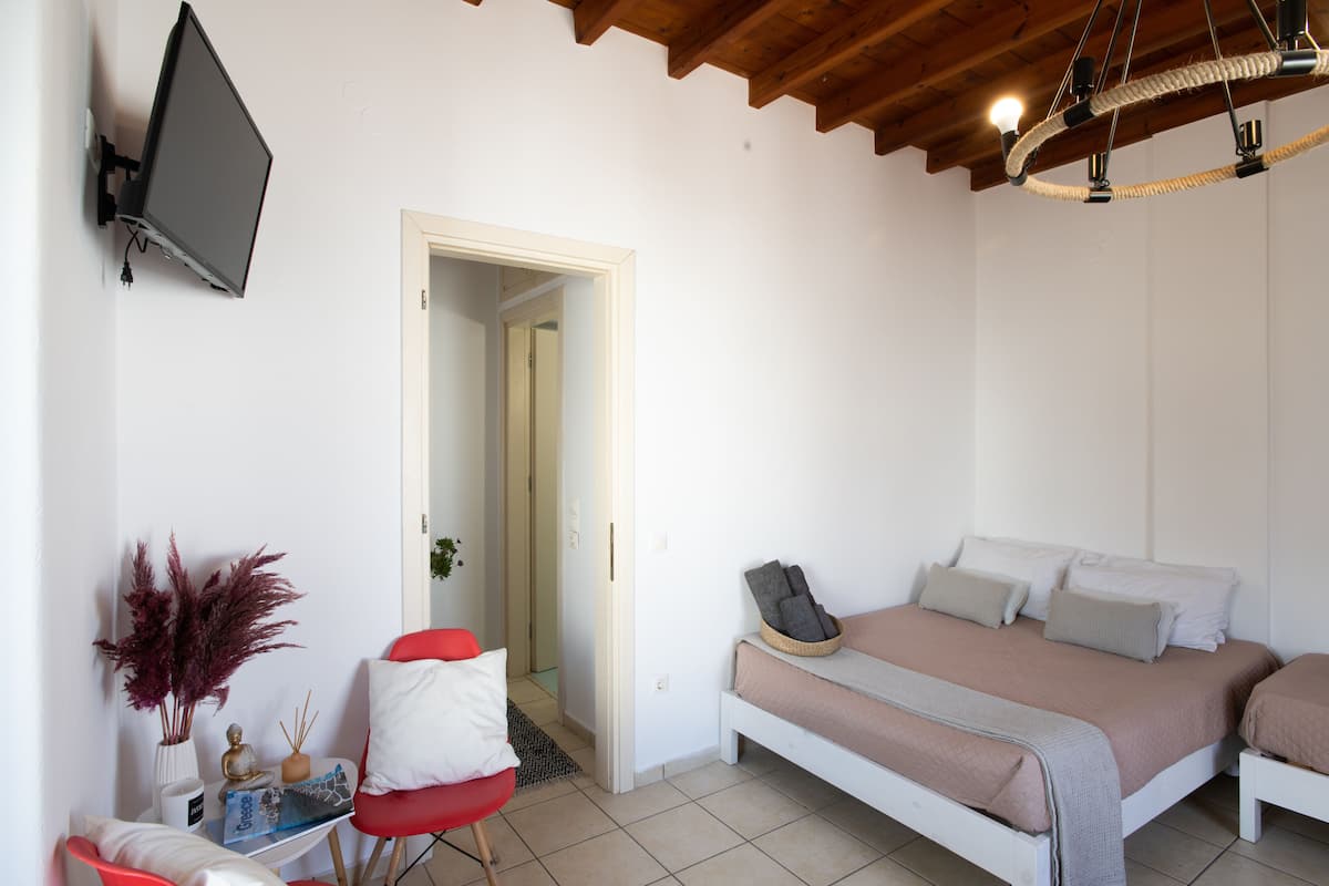 A bedroom with a bed, a TV mounted on the wall, a red chair, and a small table with decorative items.