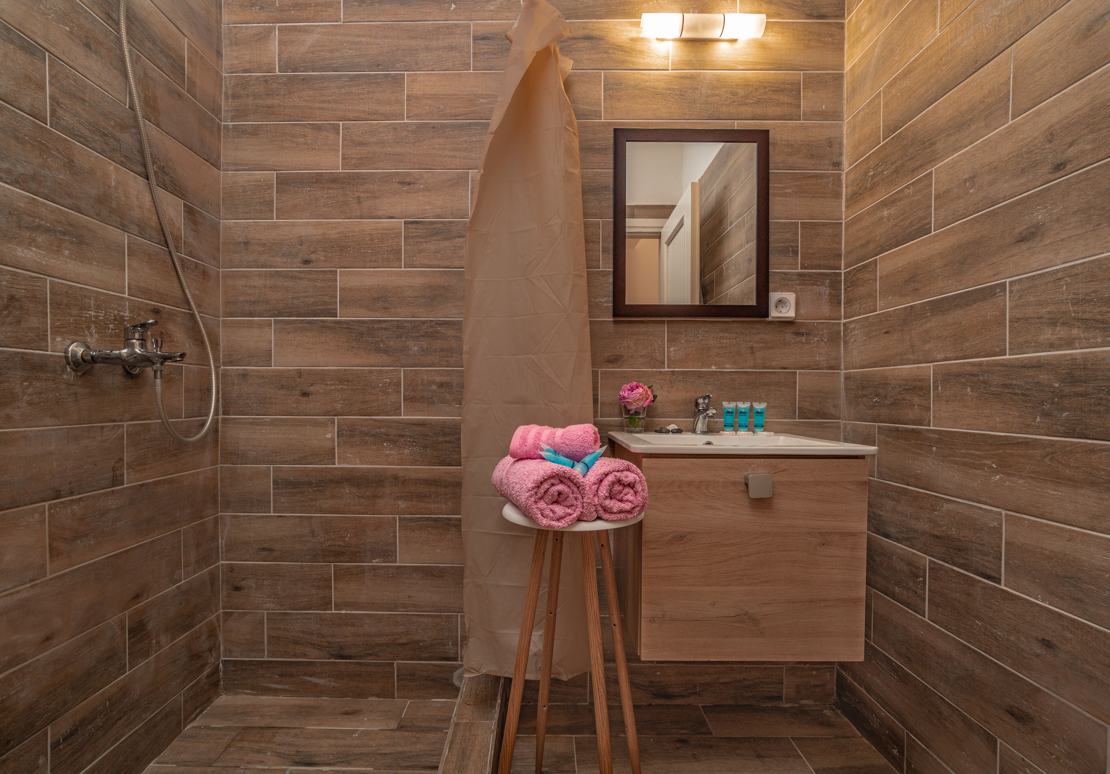 A bathroom with wooden walls, a shower, a sink with toiletries, and a mirror.