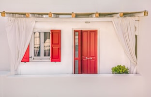 Un edificio blanco con dos puertas rojas y una ventana con contraventanas rojas.