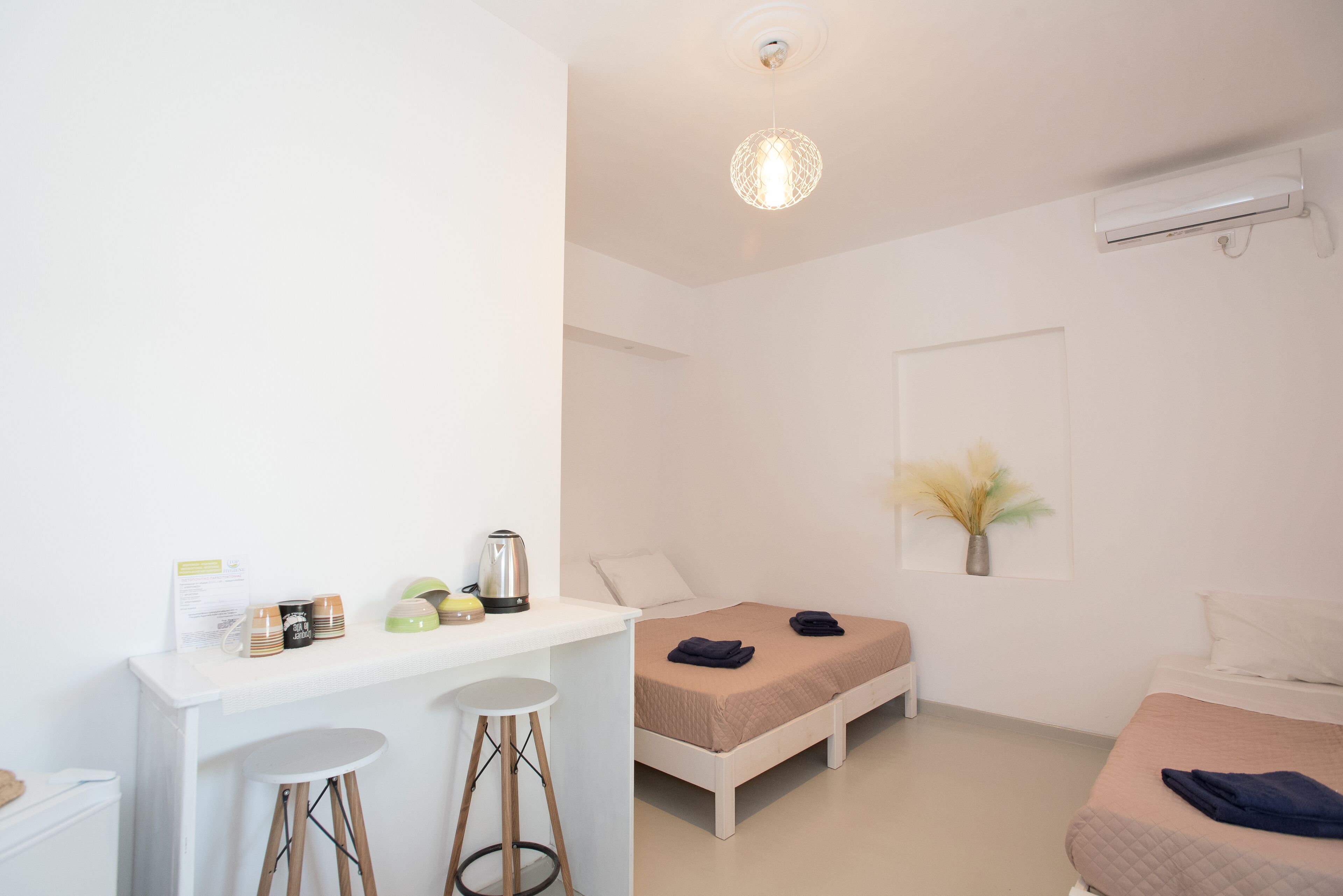 A minimalist bedroom with a bed, a desk with stools, and a small table with a kettle and mugs.