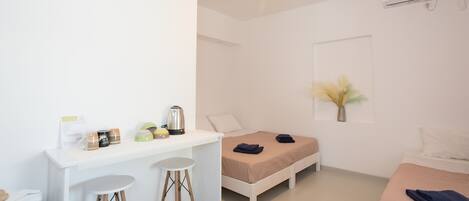 A minimalist bedroom with a bed, a desk with stools, and a small table with a kettle and mugs.