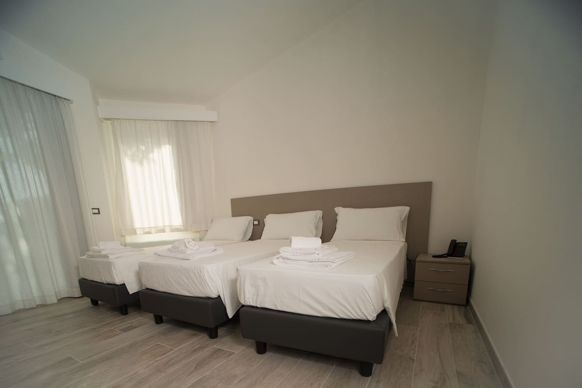 A hotel room with two beds, a bedside table with a phone, and a window with curtains.