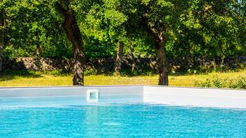 A swimming pool with clear blue water, surrounded by trees and a stone wall.