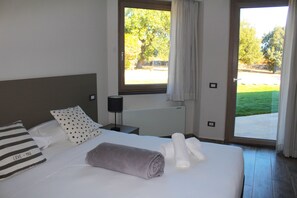 Une chambre d’hôtel avec un lit, des oreillers, une serviette roulée, une table de chevet, une lampe et une fenêtre avec des rideaux.