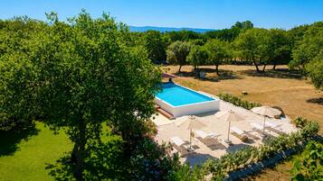 A swimming pool with a sunlit patio area, surrounded by trees and a clear sky.