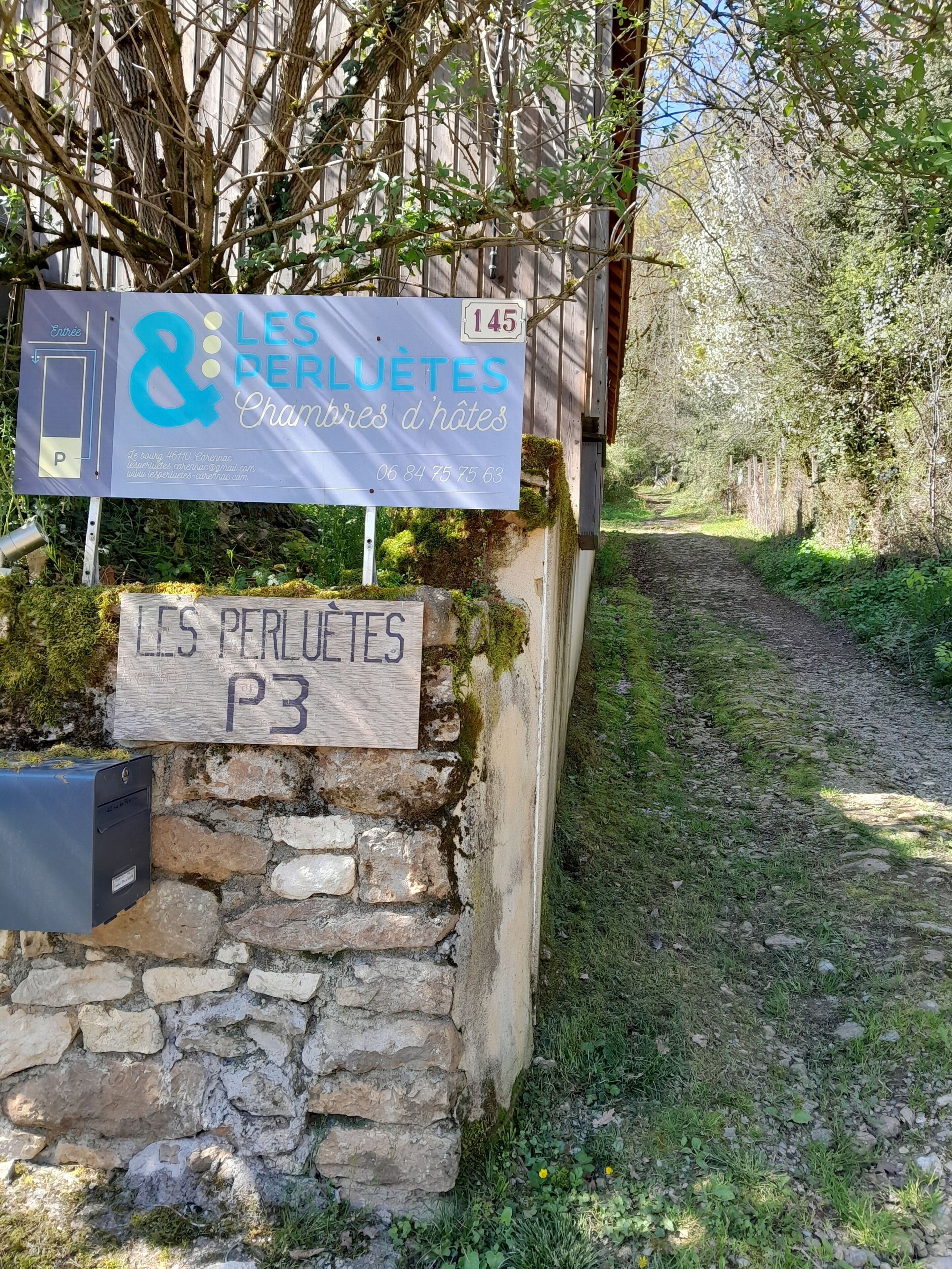 A stone wall with a sign for 'LES PERLUETES Chambres d'hôtes' and a mailbox.