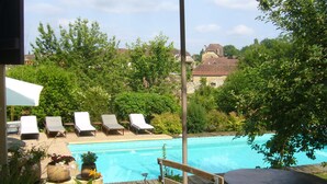 Une piscine entourée de chaises longues, avec une végétation luxuriante et des maisons en arrière-plan.