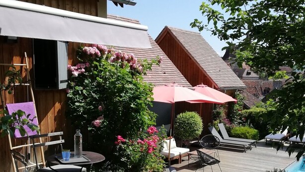 Une terrasse en bois avec des meubles d’extérieur, une pergola et un jardin fleuri.