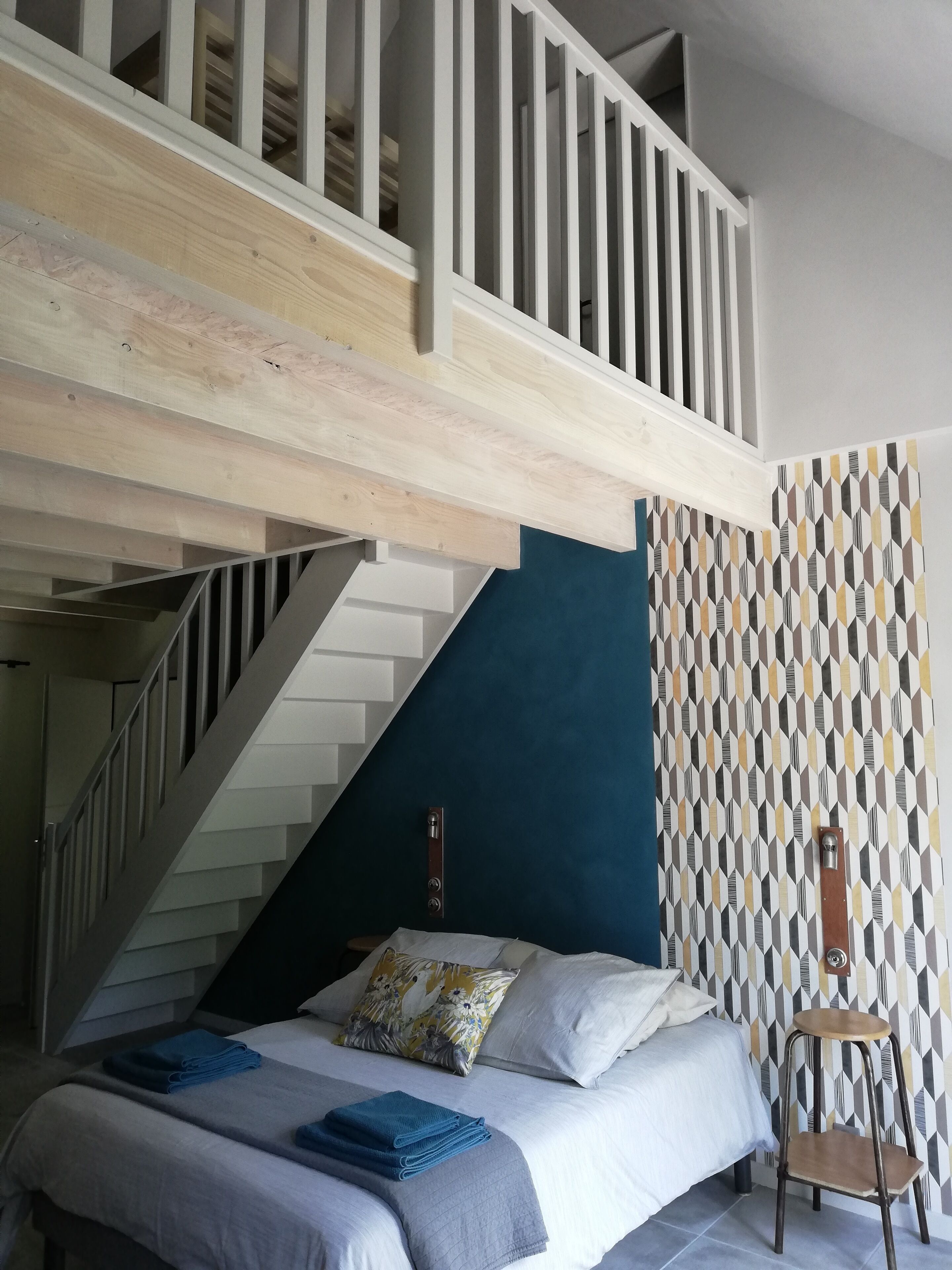 Un dormitorio con una cama, una silla, una escalera y una pared con diseño geométrico.