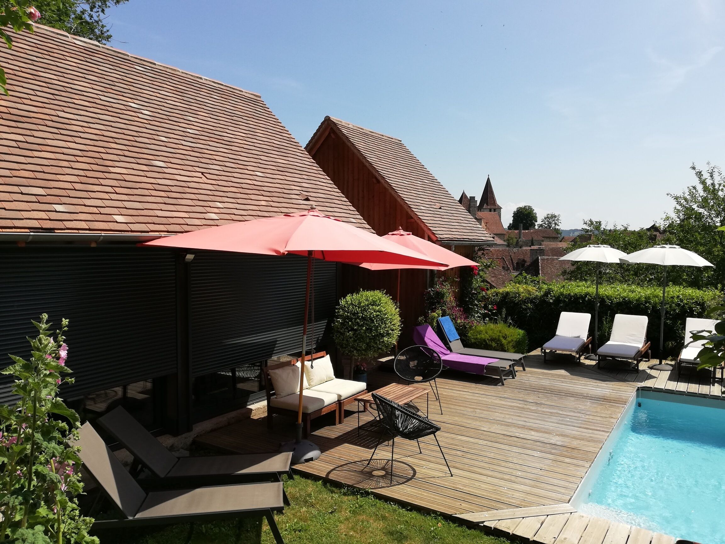 A backyard with a pool, lounge chairs, and a red umbrella.
