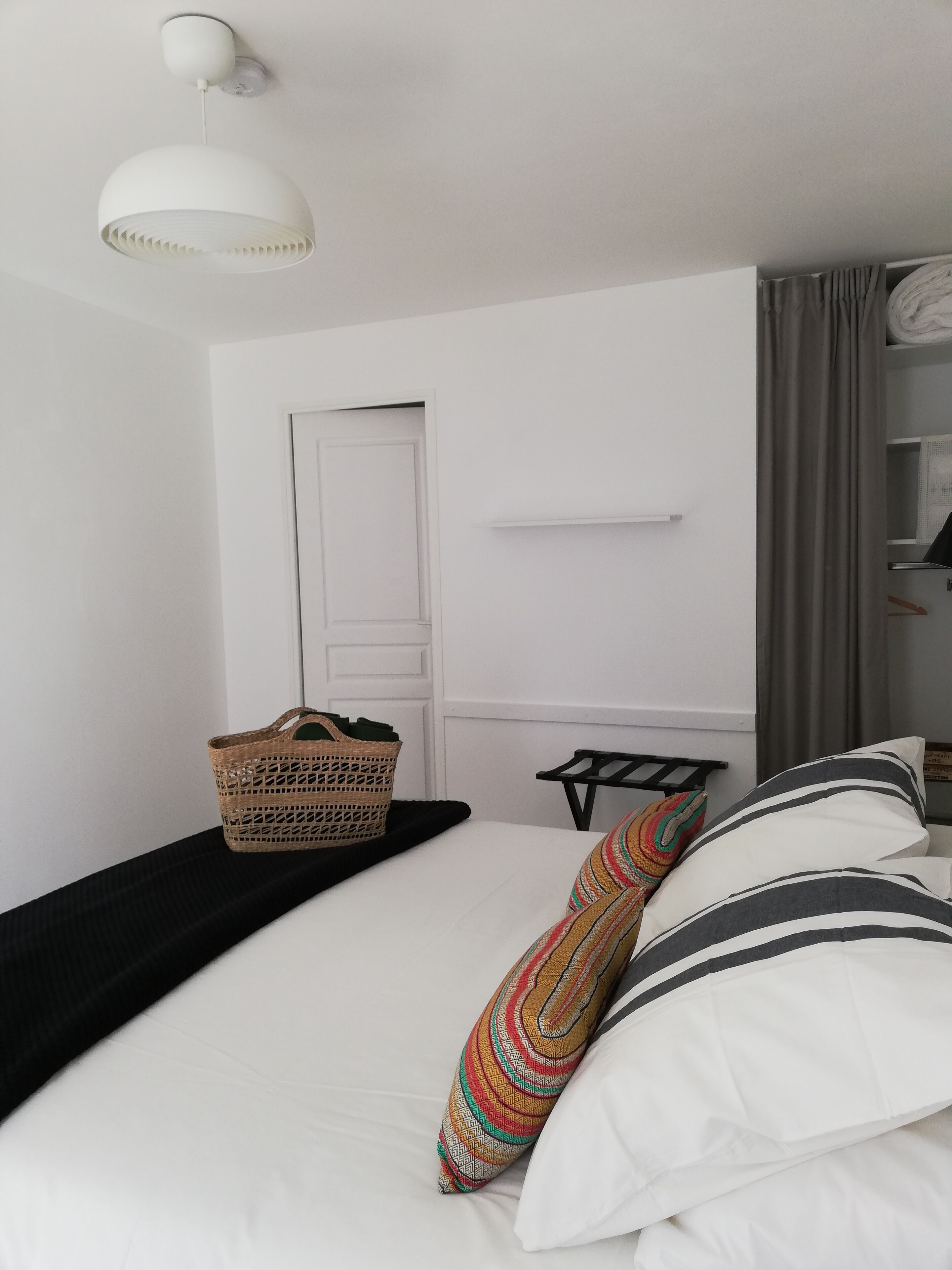Un dormitorio con cama, lámpara colgante, puerta y estante con objetos.