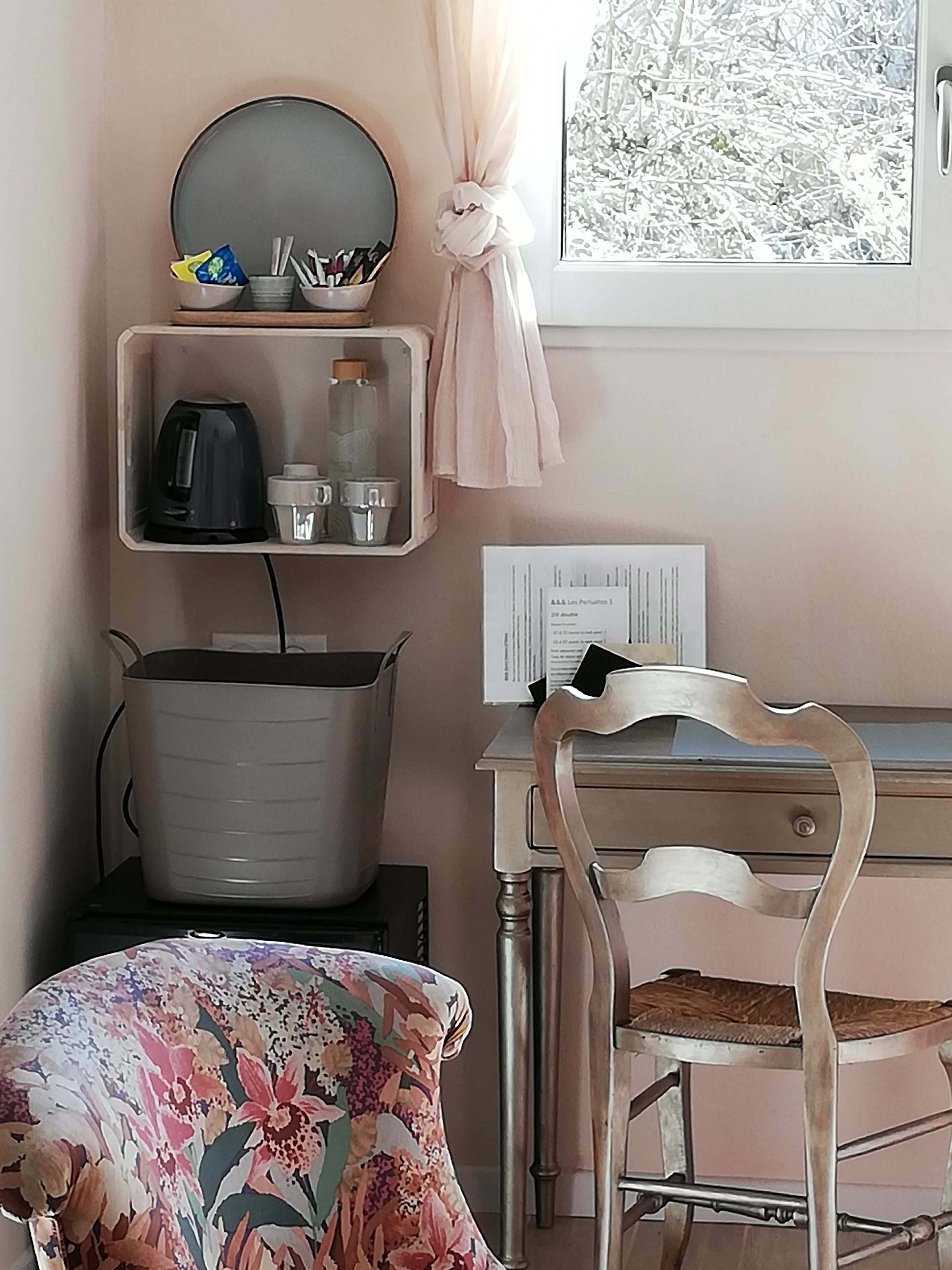 A room with a desk, chair, and a shelf with kitchen items.