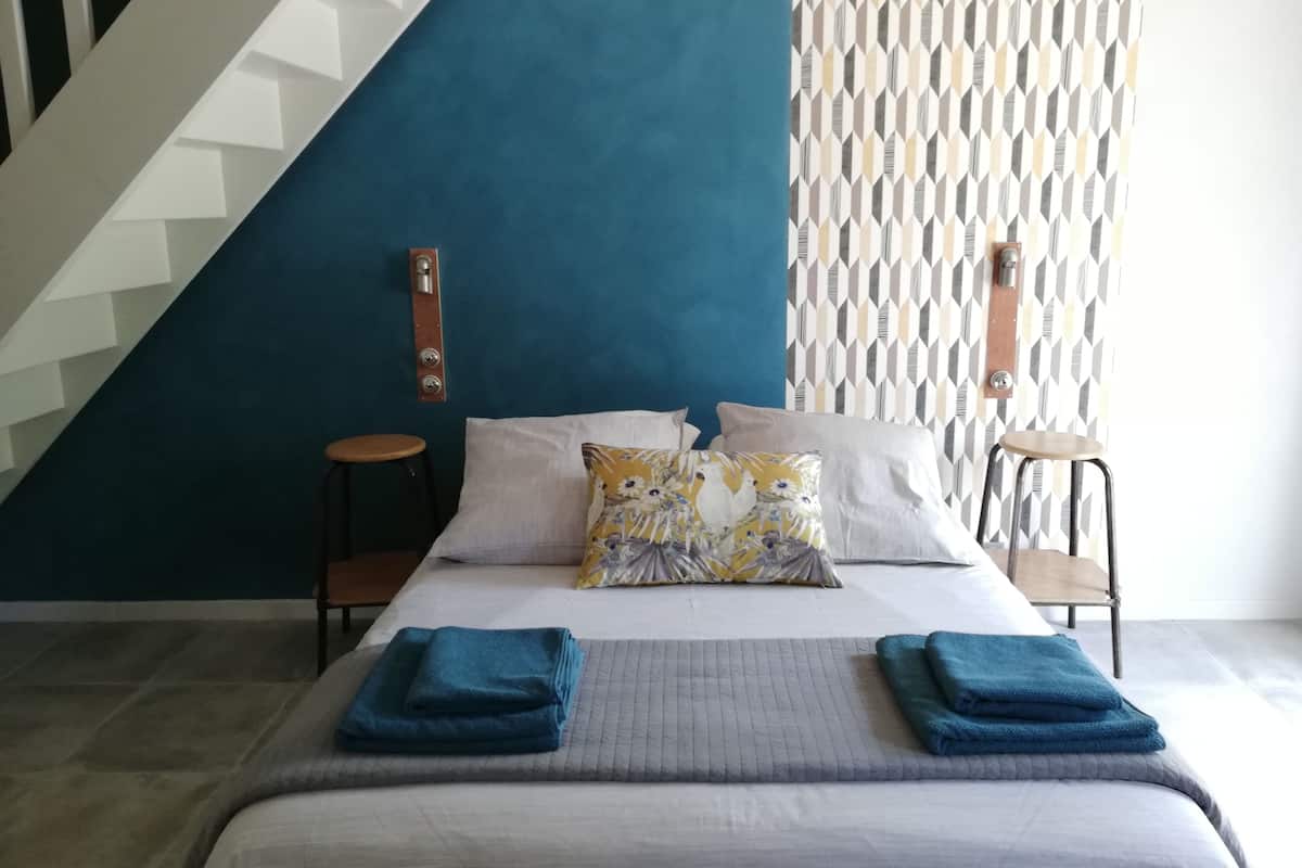 A bedroom with a bed, pillows, a nightstand, a chair, and a patterned wall.