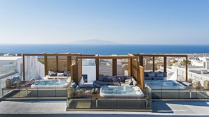 Una terraza en la azotea con dos jacuzzis, un pérgola de madera y vistas al mar y una montaña distante.