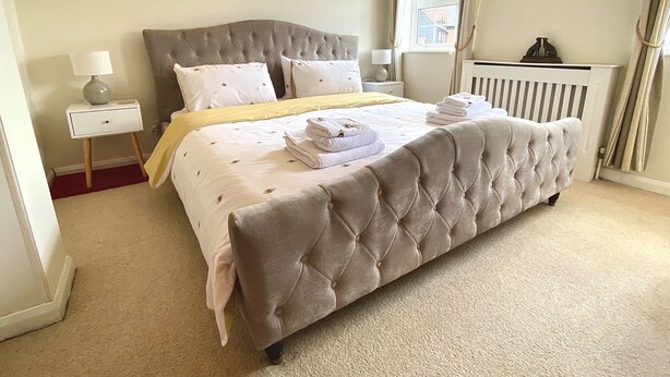 A neatly made bed with a tufted headboard, a bedside table with a lamp, and heart-shaped wall decorations. - Bumblebee Cottage - a 19th Century Cottage in Area of Outstanding Natural Beauty (Gaddesden Row)