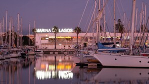 A marina with multiple boats docked, a building with 'MARINA LAGOS' signage, and calm water reflecting the boats and building. - Comfortable sea view apartment [77] (Lagos)