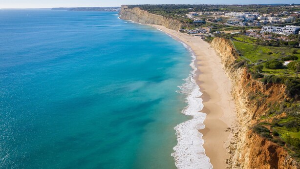 A coastal landscape with a sandy beach, cliffs, and a residential area in the background. - Comfortable sea view apartment [77] (Lagos)