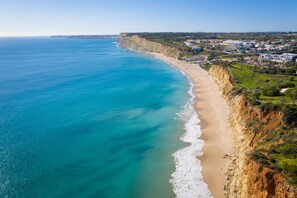 Un paisaje costero con una playa de arena, acantilados y una zona residencial al fondo.