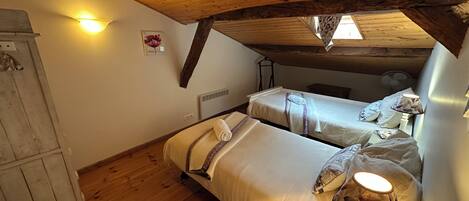 Un dormitorio acogedor en el ático con vigas de madera, dos camas, un armario y una mesita con lámpara.