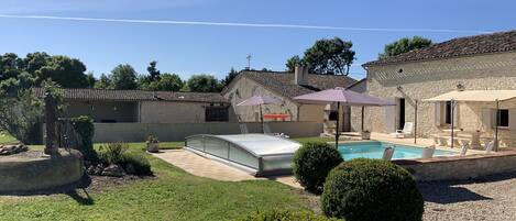 Un patio trasero con piscina, mobiliario exterior y una construcción de piedra.