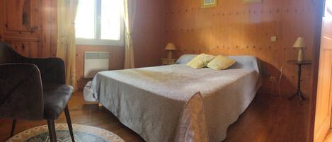 A bedroom with a bed, a chair, a table, and a radiator.