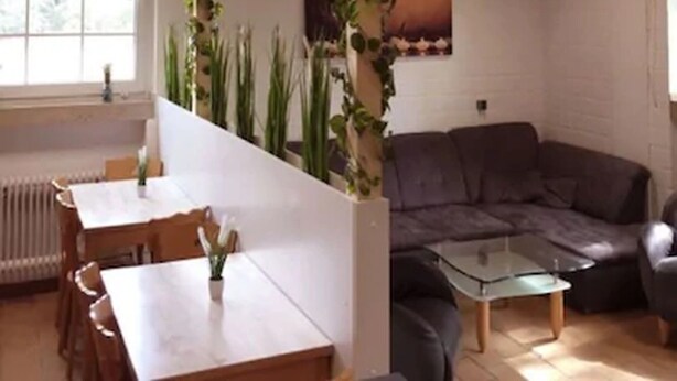 A modern living room with a wooden ceiling, a grey sofa, a glass coffee table, and a dining area with a white table and chairs. - Herberge zur Herrlichkeit (Dorsten)