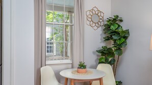A room with a round table, two chairs, a window with curtains, a wall-mounted decorative item, and a potted plant.