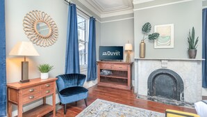 A living room with a fireplace, a blue velvet chair, a wooden side table, and a blue sofa.