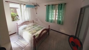 Een slaapkamer met een bed, een raam met gordijnen, een plafondventilator en een deur.
