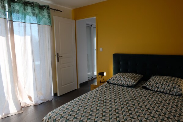 Un dormitorio con cama, almohadas, una mesita de noche y una puerta que da a otra habitación.