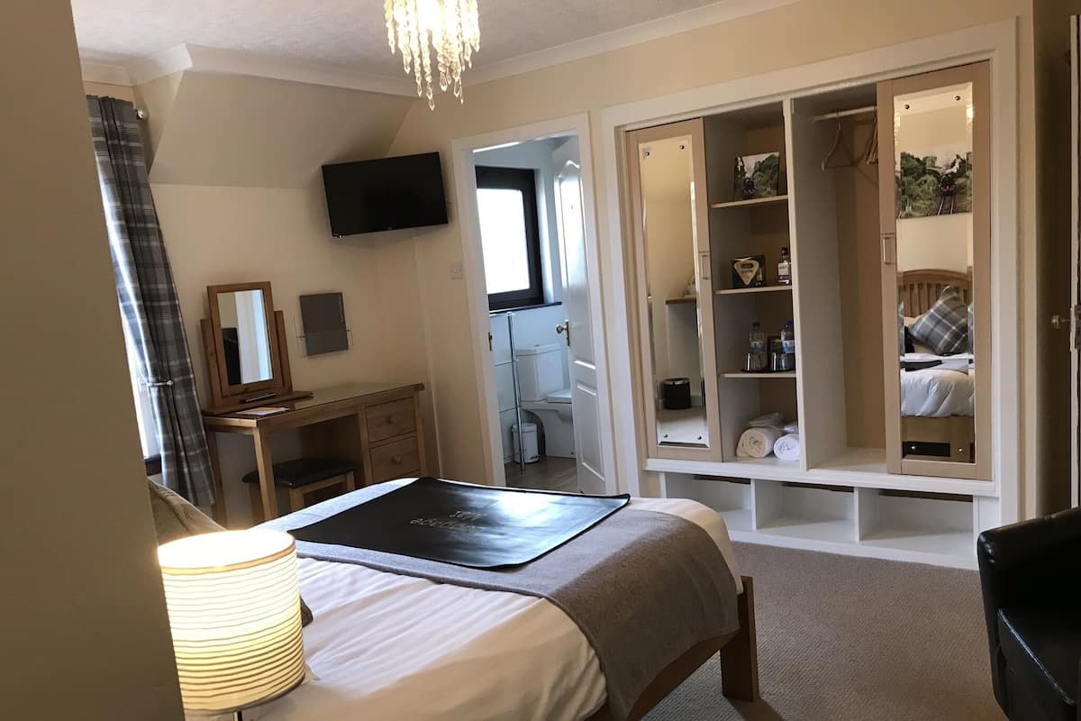 Ein Schlafzimmer mit Bett, Nachttisch, Lampe, Kleiderschrank und einem Fernseher an der Wand.