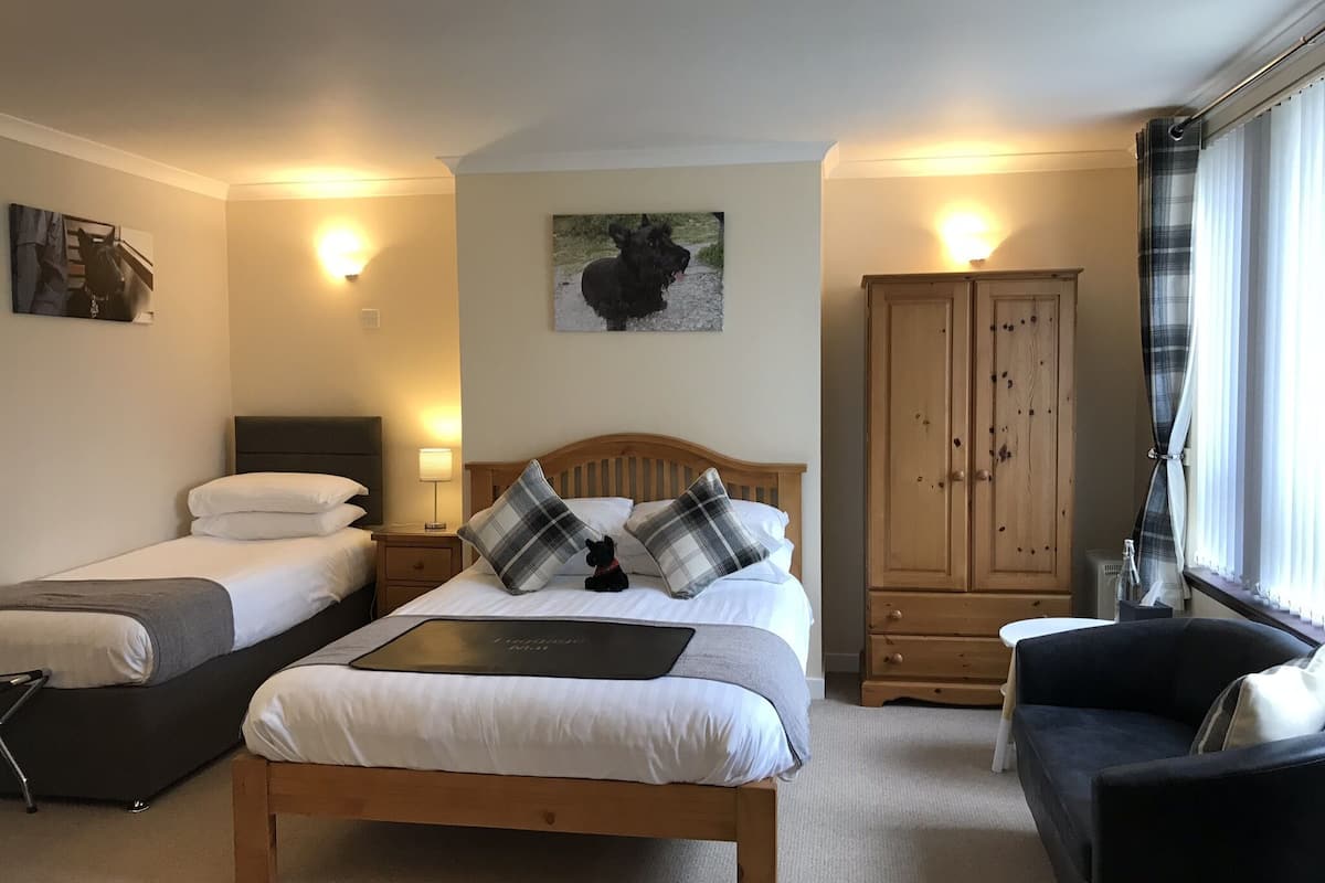 Ein Schlafzimmer mit zwei Einzelbetten, einem größeren Bett mit Kopfteil, einem Kleiderschrank, einem Nachttisch, einer Lampe und einem Fenster mit Vorhängen.