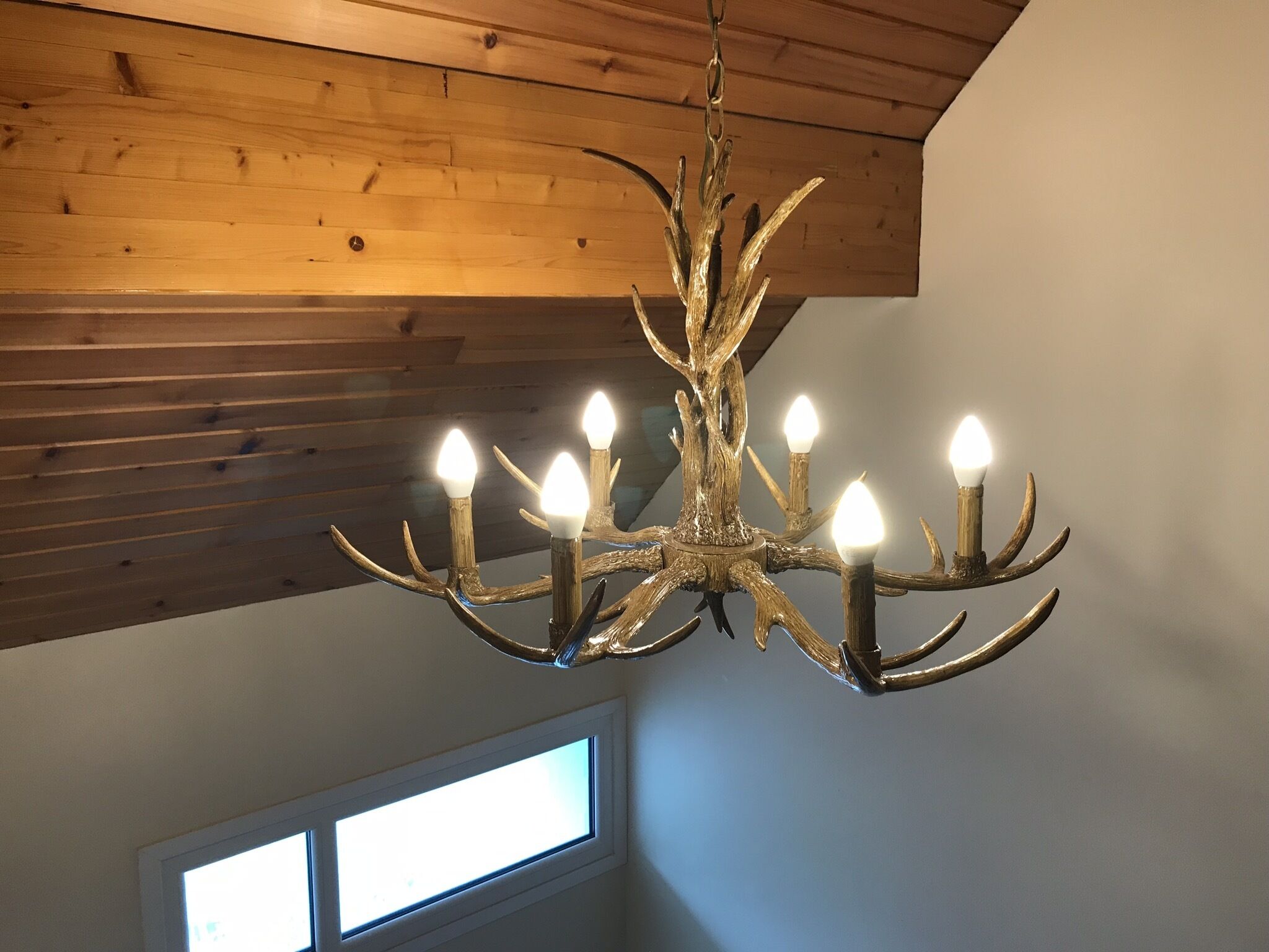A chandelier with multiple lights, wooden ceiling beams, and a window with natural light.