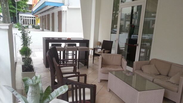 A sunlit patio with wicker furniture, a glass table, and potted plants. - Hotel Cuba Rimini (Rimini)