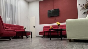 A modern living room with a red sofa, a white armchair, and a flat-screen TV mounted on a red wall. - Hotel Cuba Rimini (Rimini)