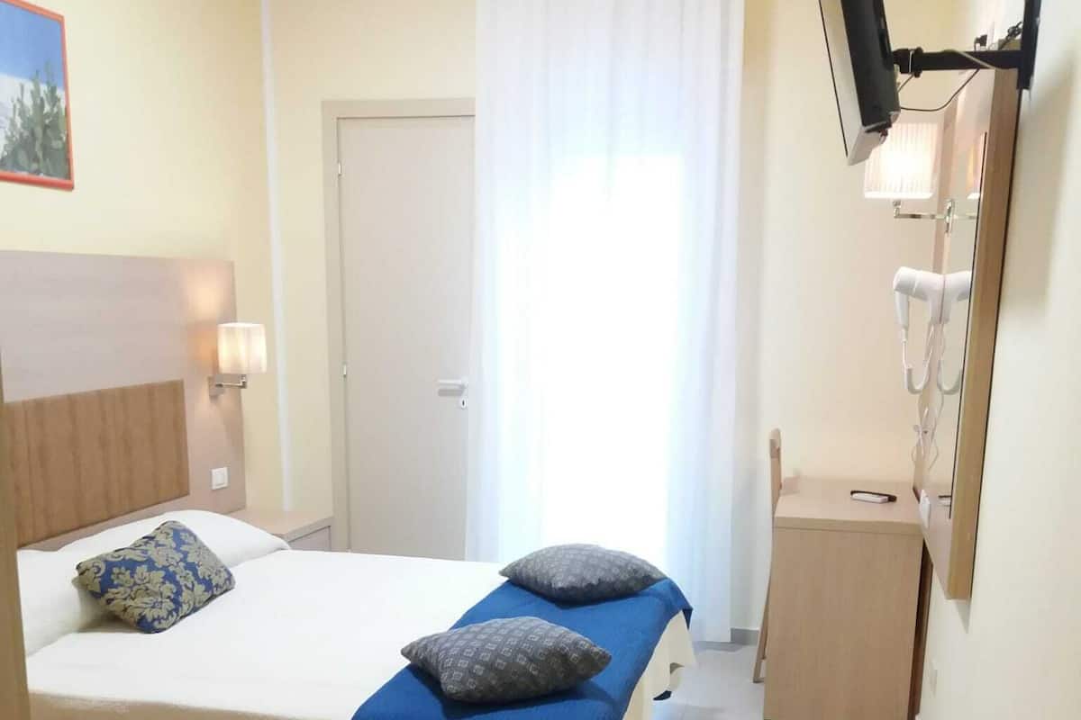 Una camera d'albergo con un letto, un comodino, uno specchio e una TV a parete.