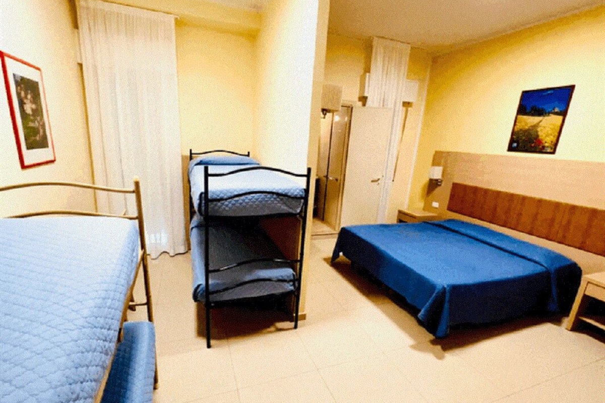 Una stanza con letti a castello, un letto singolo, una porta, un tavolino e un quadro appeso al muro.