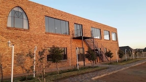 A two-story brick building with large windows, a fire escape, and small trees along the sidewalk. - WCCC Convention Centre (Roodepoort)