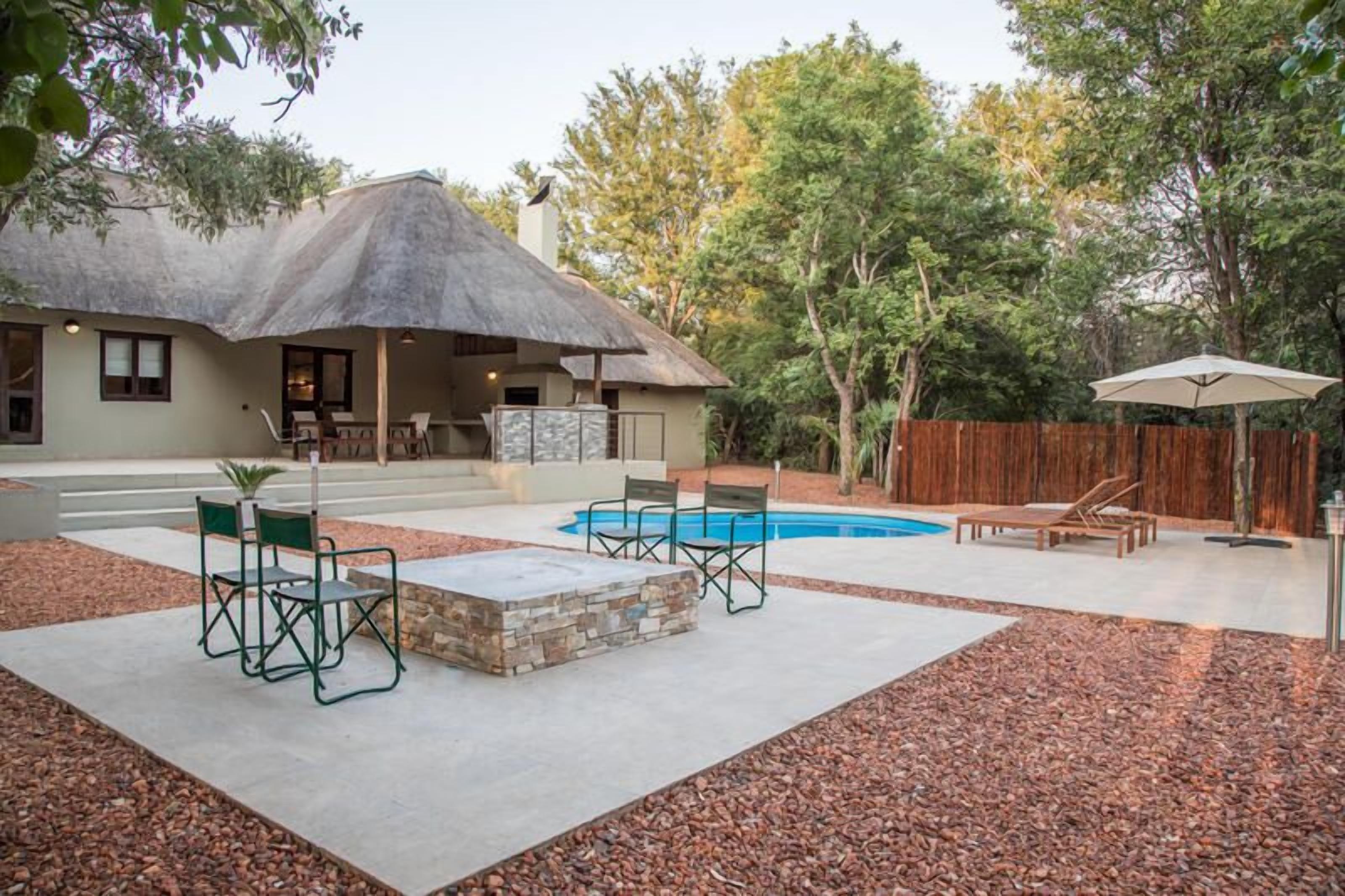 Un patio trasero con piscina, mobiliario exterior y una construcción con techo de paja.