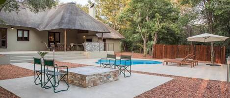 A backyard with a swimming pool, outdoor furniture, and a thatched-roof building.