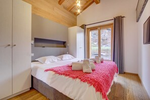 A bedroom with a bed, white linens, a red throw blanket, and a window with curtains.