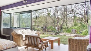 A room with wicker furniture, a bed, a sofa, and a table. There is a large window providing a view of the outdoors.