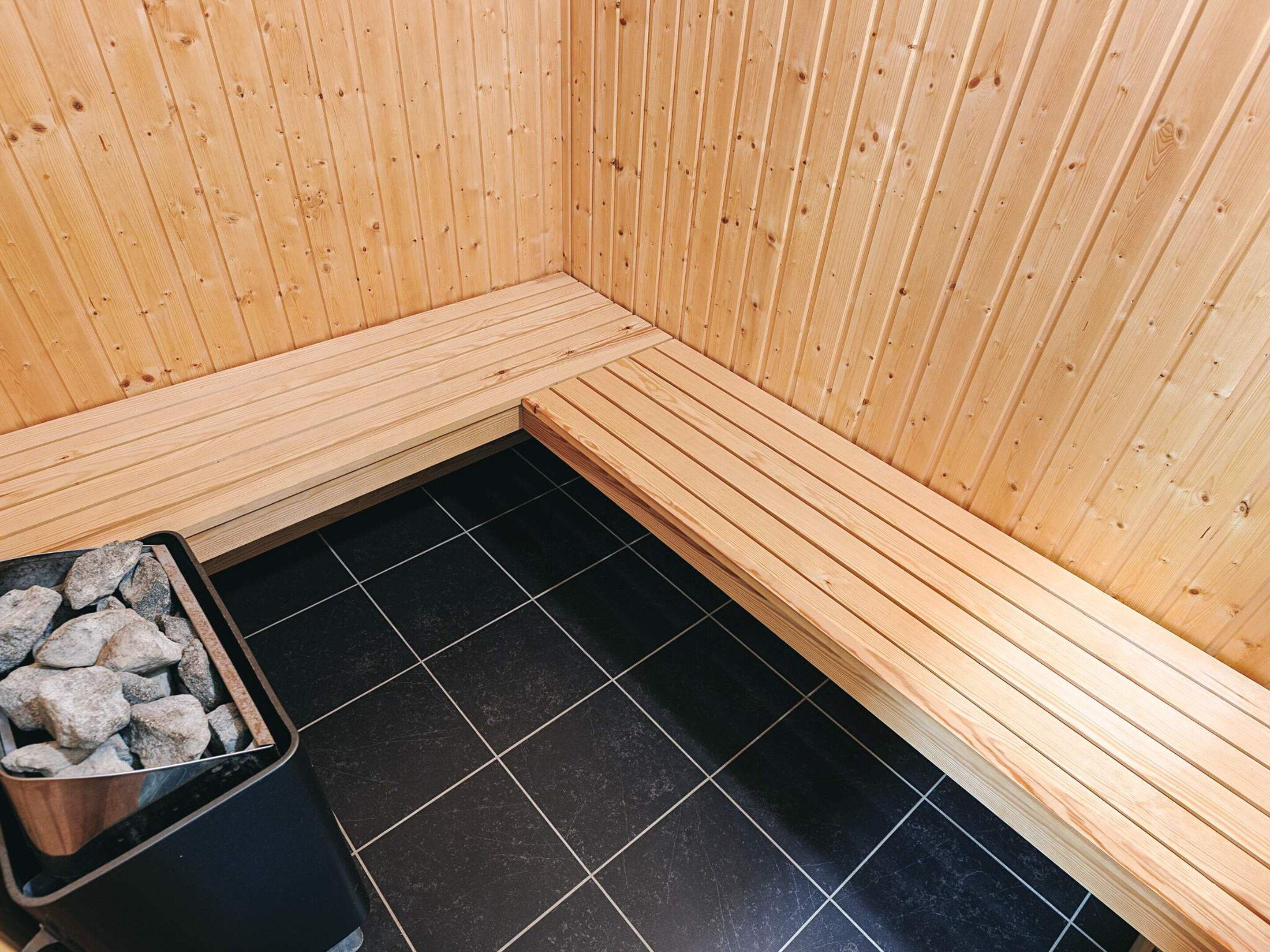 A sauna room with wooden walls, a bench, and a black tiled floor.