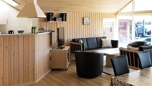 Un intérieur moderne avec un plafond en bois, un coin cuisine doté d’un comptoir, un canapé noir, une table basse et une table à manger avec des chaises.