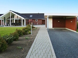 Un bâtiment doté d’un espace extérieur aménagé avec une zone de repos couverte, d’une allée en gravier et d’un jardin paysager.