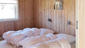Une pièce aux murs recouverts de lambris en bois, un lit avec une literie blanche et une fenêtre équipée de stores.