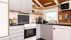 Una cocina compacta con armarios blancos, salpicadero de baldosas negras y suelo de madera.