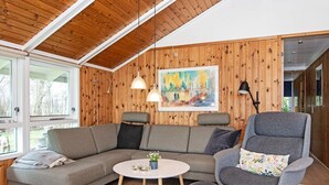 Una sala moderna con techo de madera, un sofá seccional gris, un sillón gris y una mesa de centro redonda.